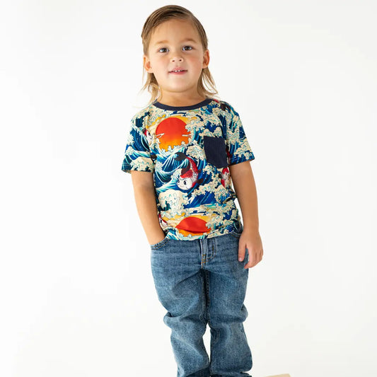 Child wearing a colorful graphic t-shirt with a sunset and fish design on a white background