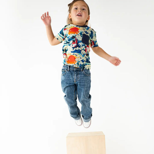 Child wearing a colorful shirt and blue jeans jumping on a white background