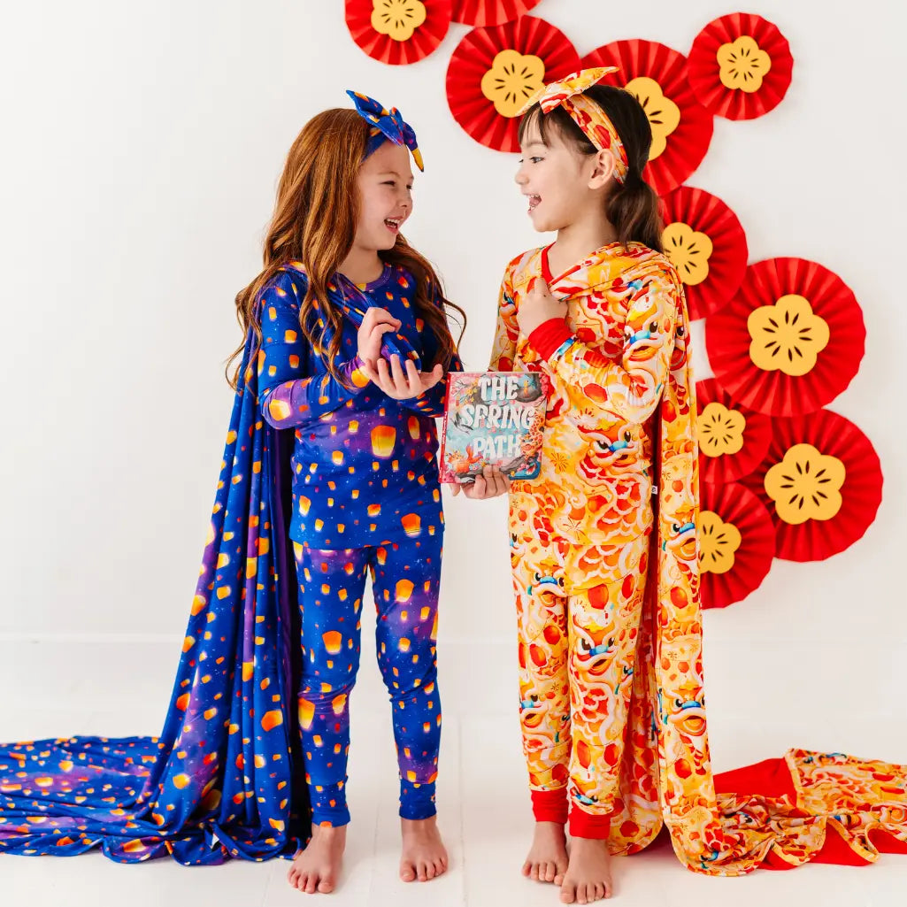 Two children in colorful pajamas standing in front of decorative flowers, holding a book.