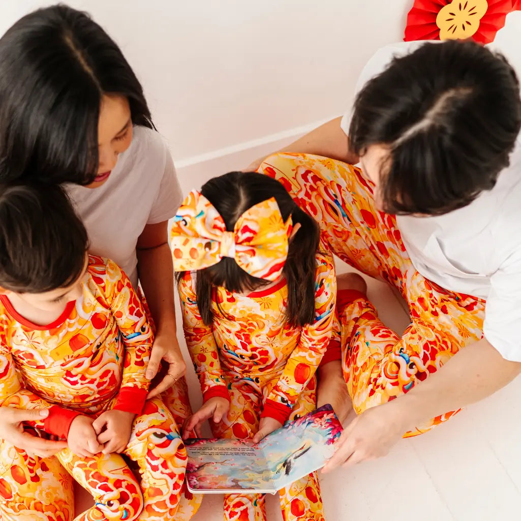 Family of four in matching pajama sets reading a book together.