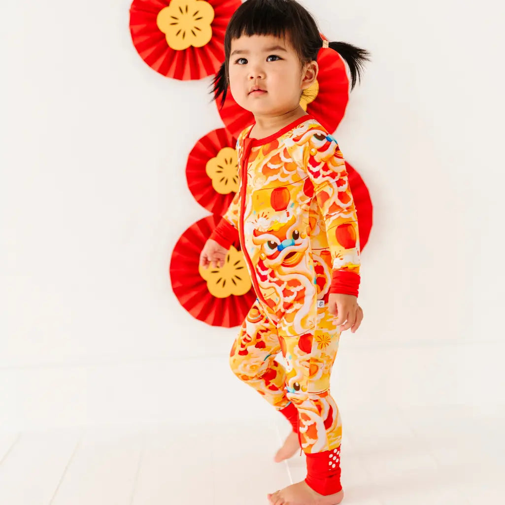 Child wearing a colorful dragon-themed onesie with red fans in the background