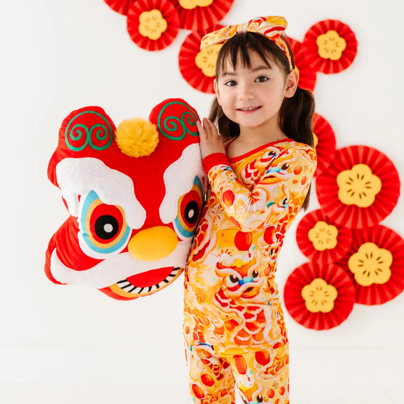 Child in traditional Chinese outfit with lion dance costume and red floral decorations on a white background