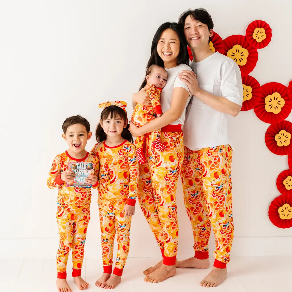 Family of five wearing matching orange and red pajamas with a decorative floral wall in the background.