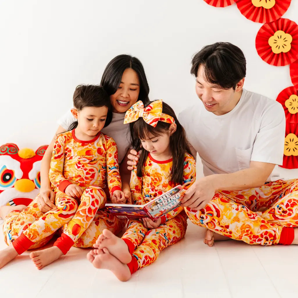 Family of four wearing matching orange and red outfits with a child reading a book.