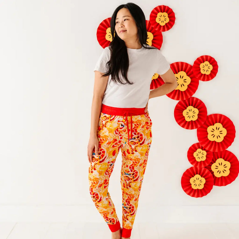 Person wearing a white t-shirt and orange floral pants with red accents, standing against a white background with decorative red and yellow elements.