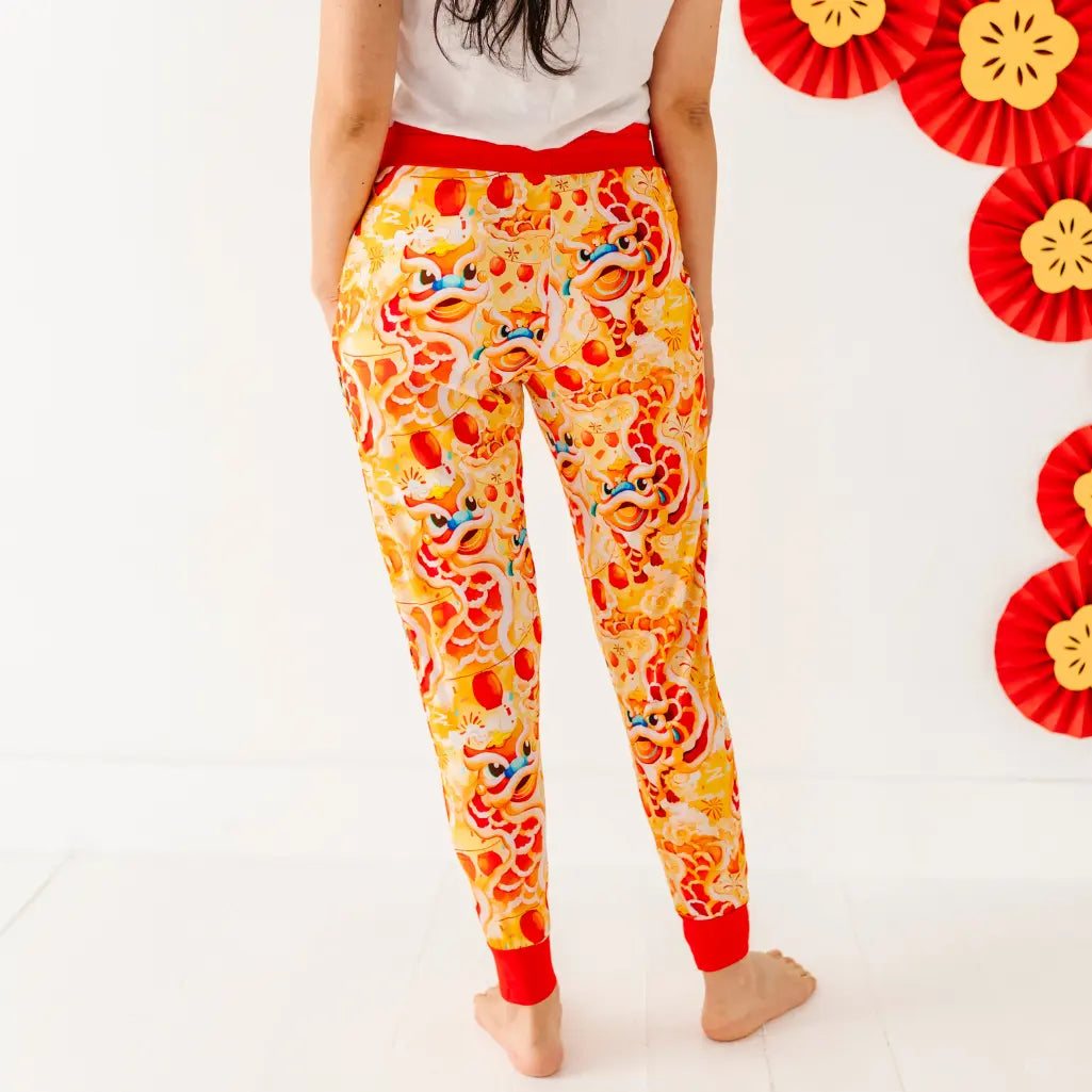 Person wearing colorful pajama pants with a white background and decorative ribbons.