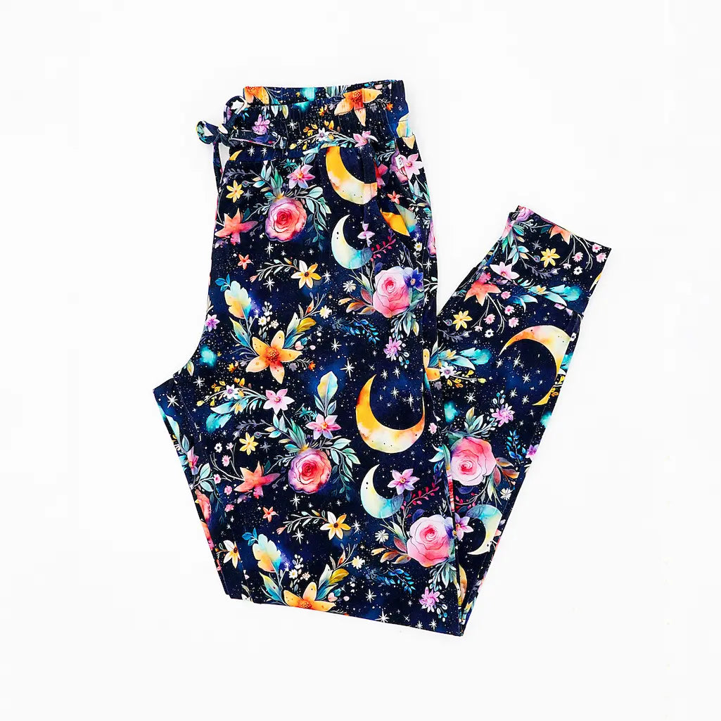 A pair of women's pajama pants with a pattern of shimmering leaves and glowing flowers, featuring a dark background and a comfortable elastic waistband.