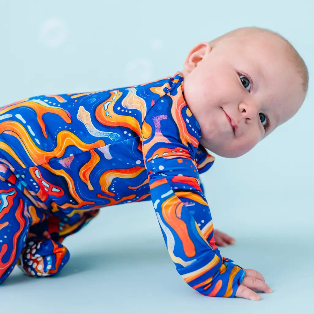 Baby wearing a colorful abstract patterned onesie on a blue background.