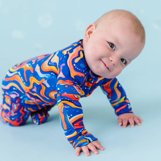 A baby in a colorful long-sleeved onesie with a fish pattern in blue and orange, resembling the appearance of Kai the Mandarin Fish.