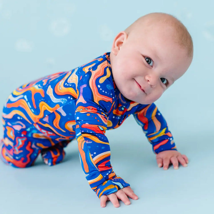 A baby in a colorful long-sleeved onesie with a fish pattern in blue and orange, resembling the appearance of Kai the Mandarin Fish.