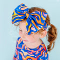 A child with red hair is wearing a blue and orange swirled bow headband.