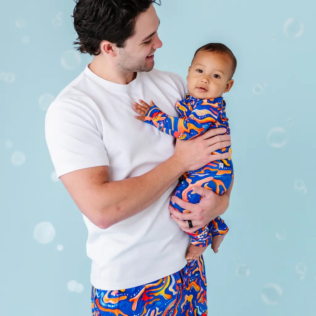 Man holding a baby both wearing colorful outfits against a light blue background.