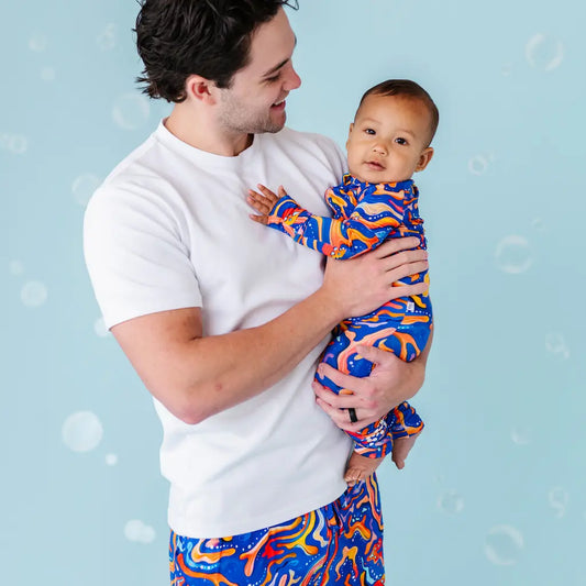 Man holding a baby both wearing colorful outfits against a light blue background.