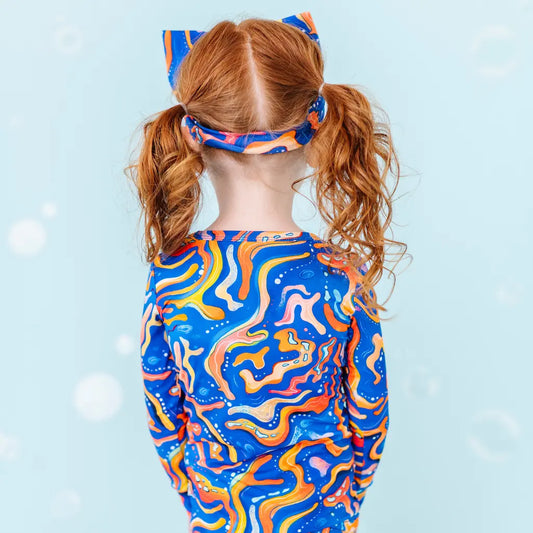 Child wearing a colorful abstract-patterned swimsuit and headband against a light blue background.