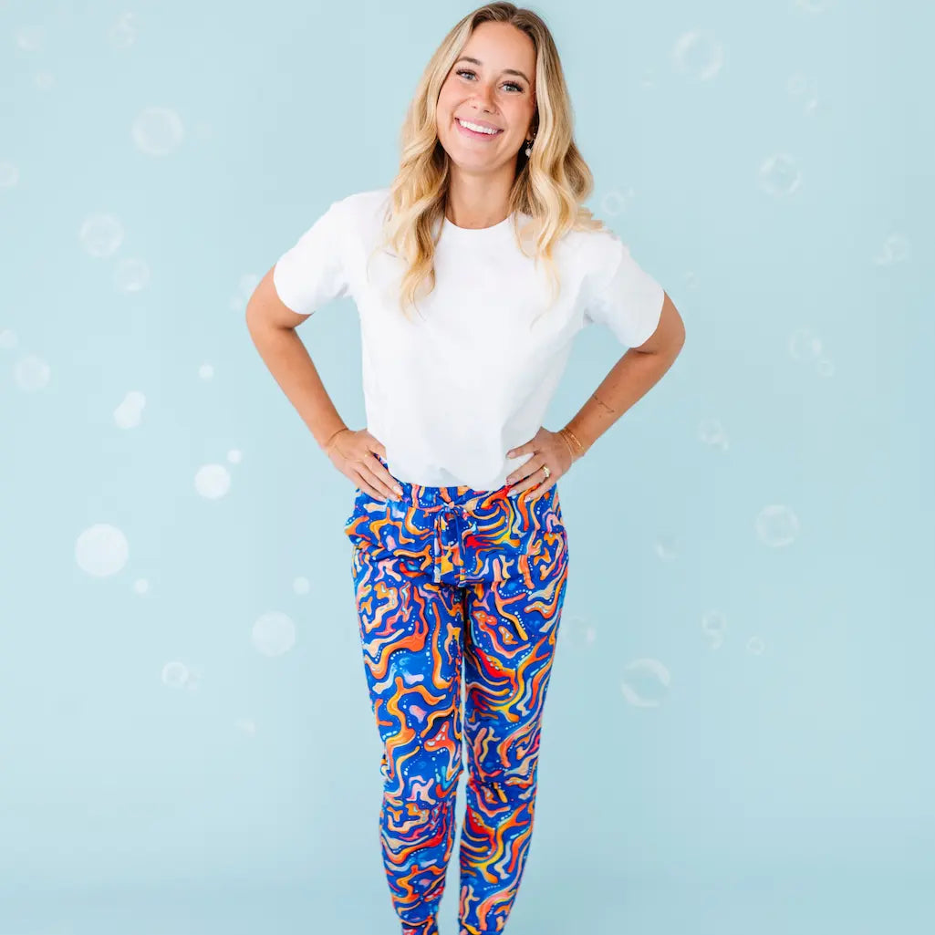 Woman wearing a white t-shirt and colorful patterned pants on a light blue background.
