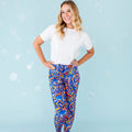 A woman standing and posing with one hand on her hip, wearing white shirt and multicolored pajama pants with a maze-like pattern in blue and orange.