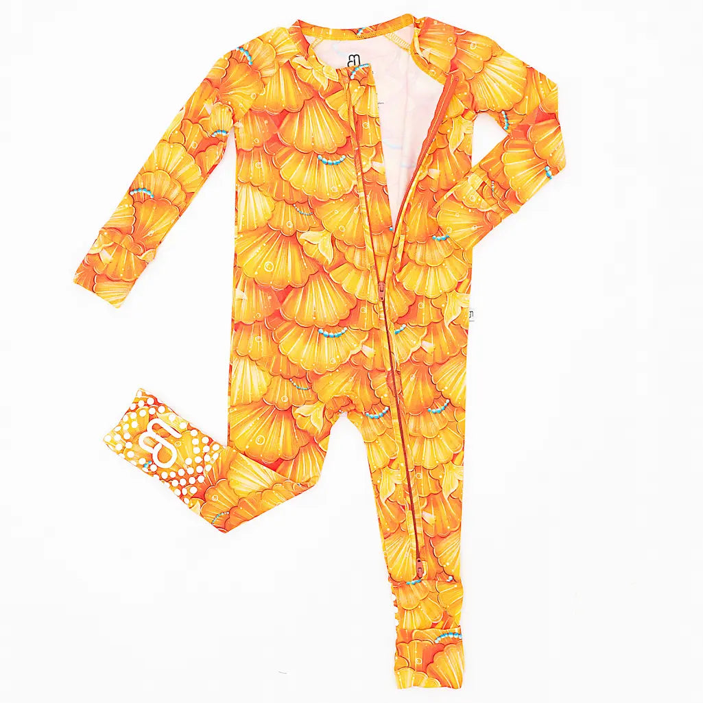A one-piece zipper pajama for babies with a mermaid pattern of golden seashell scales, and convertible foot covers.