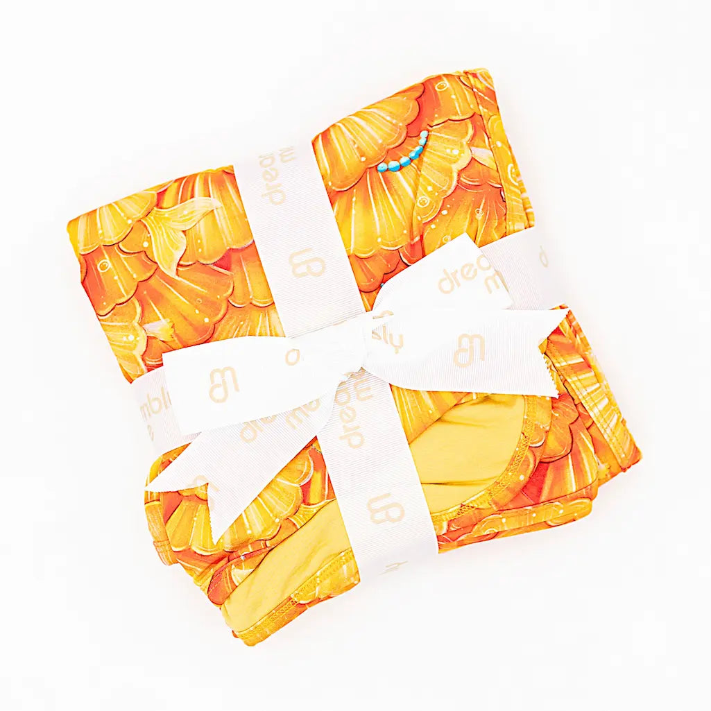 A blanket with a mermaid pattern of golden seashell scales and turquoise pearls, wrapped with a white ribbon.