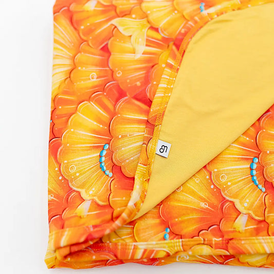 Close-up of a blanket with a mermaid pattern, showcasing a vibrant orange and yellow color theme with a golden winged sea fairy character.