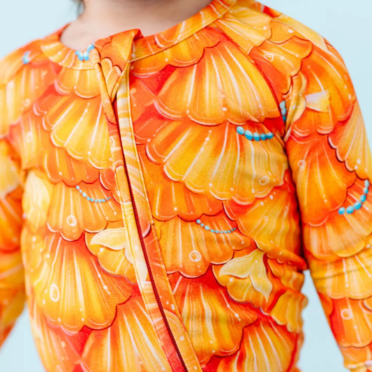 Baby wearing a colorful orange and yellow patterned onesie against a light blue background