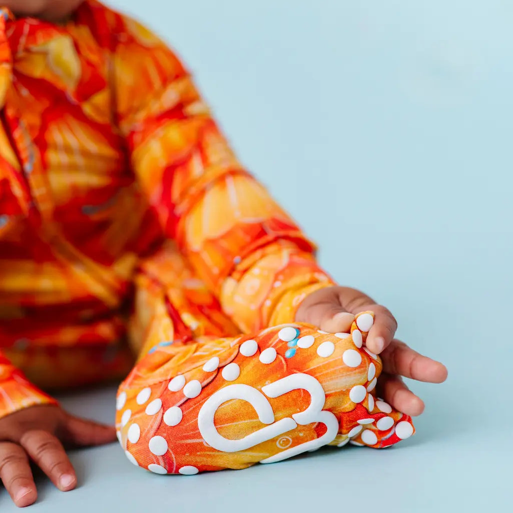 Child in orange and red tie-dye shirt holding a colorful object with white polka dots on a light blue background