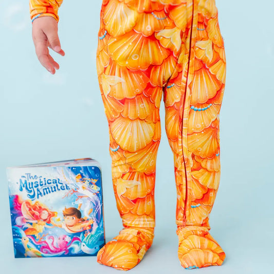 Child wearing a shell-patterned onesie with a book titled 'The Mystical Amulet' on a light blue background.