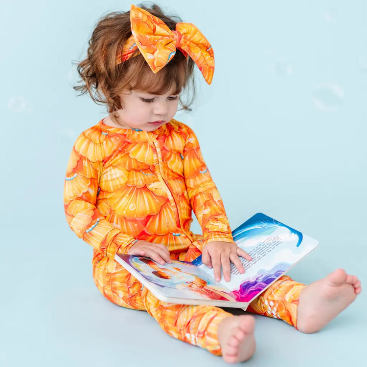 Child in orange and yellow outfit reading a book on a light blue background