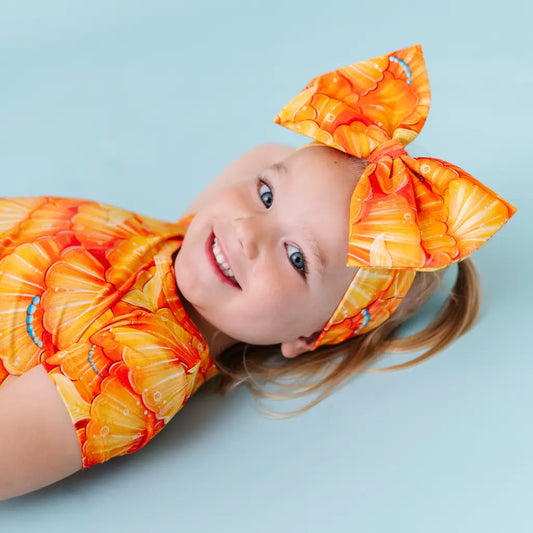 A child wearing a headband with a mermaid pattern of golden seashell scales and turquoise pearls.