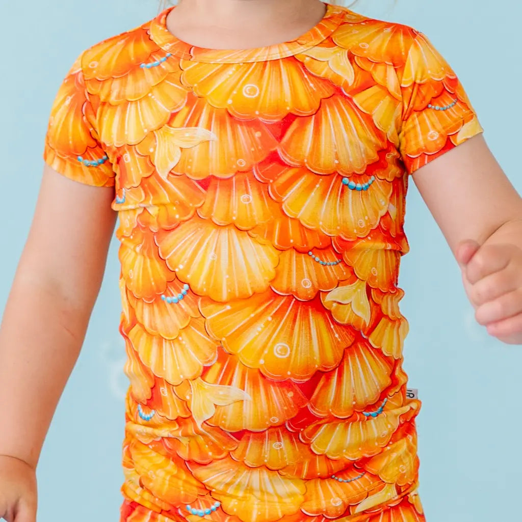 Child wearing a bright orange and yellow shell-patterned dress against a light blue background