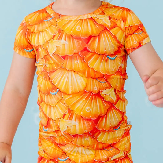 Child wearing a bright orange and yellow shell-patterned dress against a light blue background