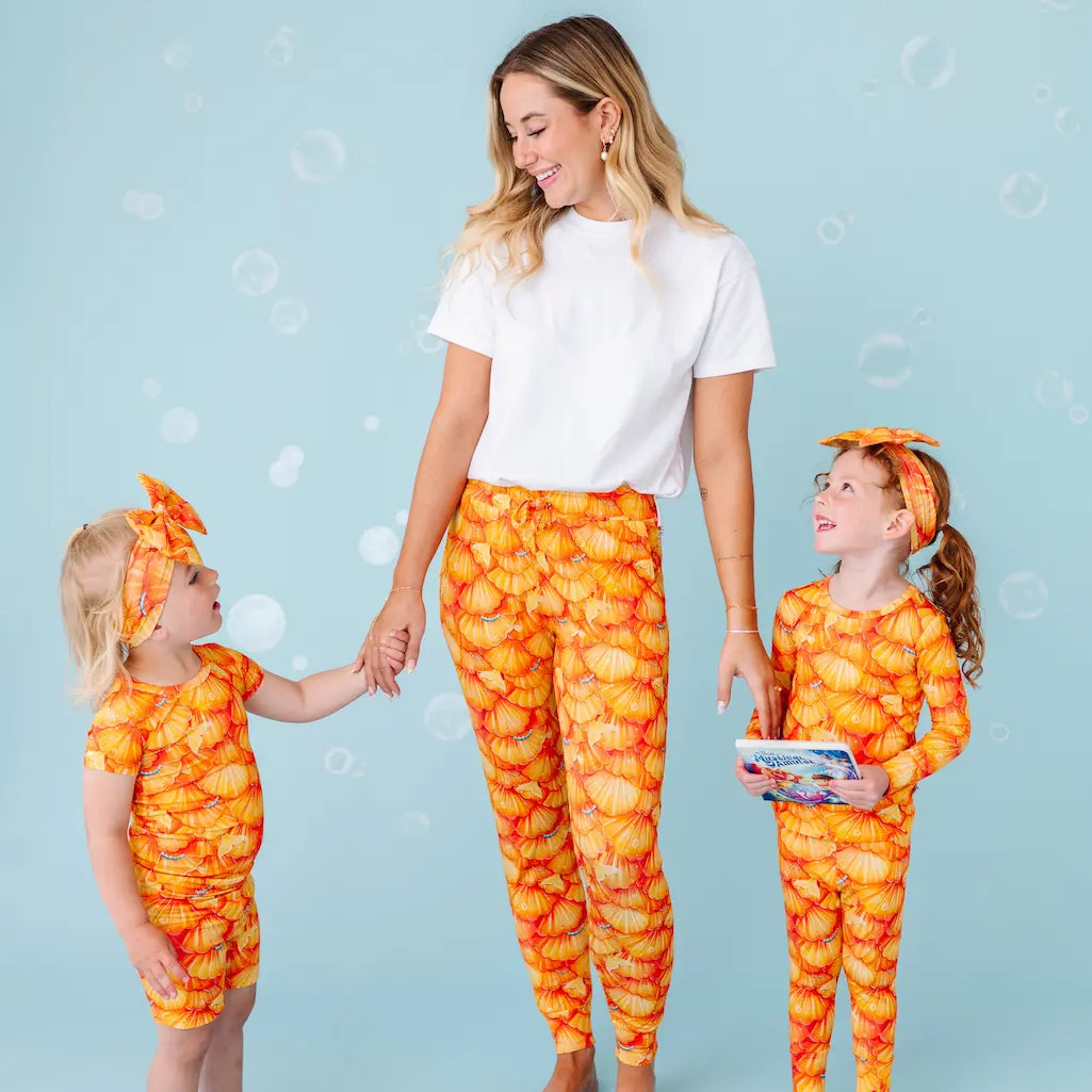 Woman and two children in matching orange and yellow outfits on a light blue background.