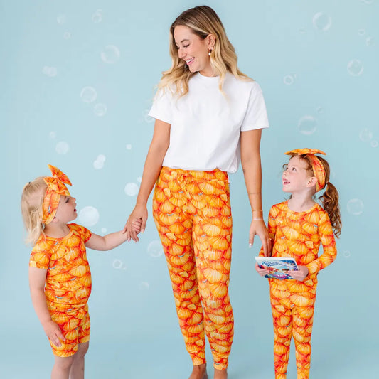 Woman and two children in matching orange and yellow outfits on a light blue background.