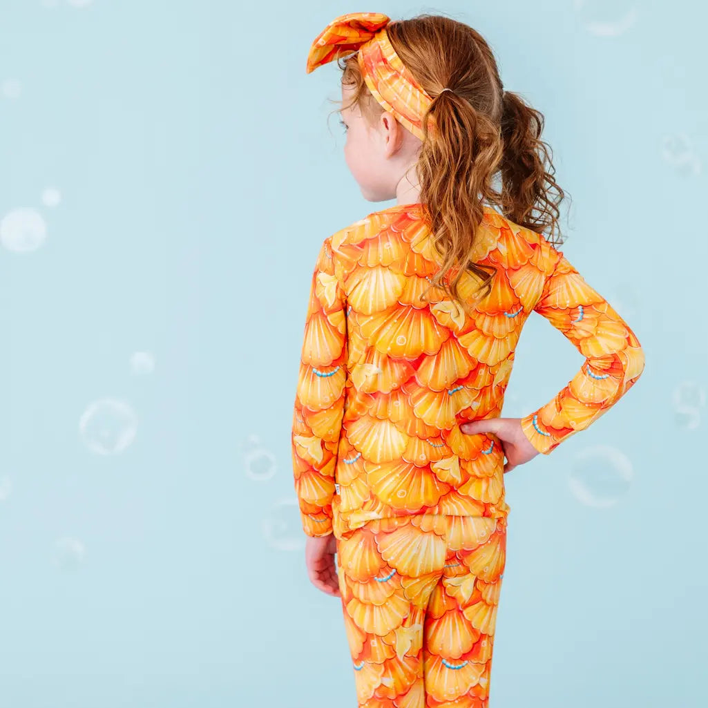 Child wearing an orange shell-patterned swimsuit on a blue background.