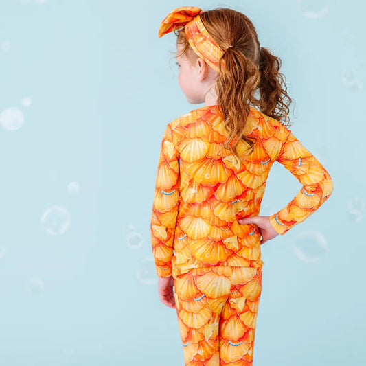 Child wearing an orange shell-patterned swimsuit on a blue background.