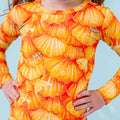 Child wearing a long-sleeve shirt with an orange shell pattern against a light blue background
