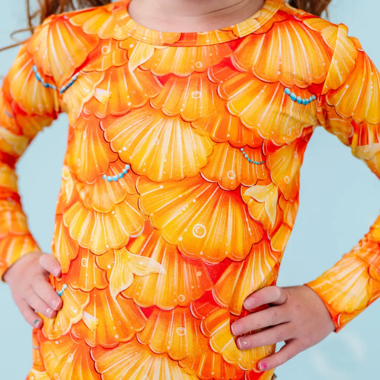 Child wearing a long-sleeve shirt with an orange shell pattern against a light blue background