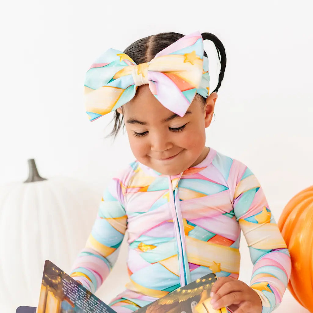 Child wearing a colorful patterned outfit and headband, holding a book.
