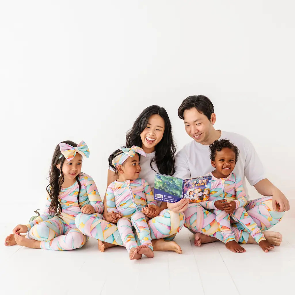 Family of four reading a book together in matching pajamas on a white background