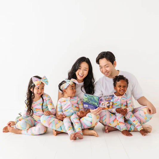 Family of four reading a book together in matching pajamas on a white background