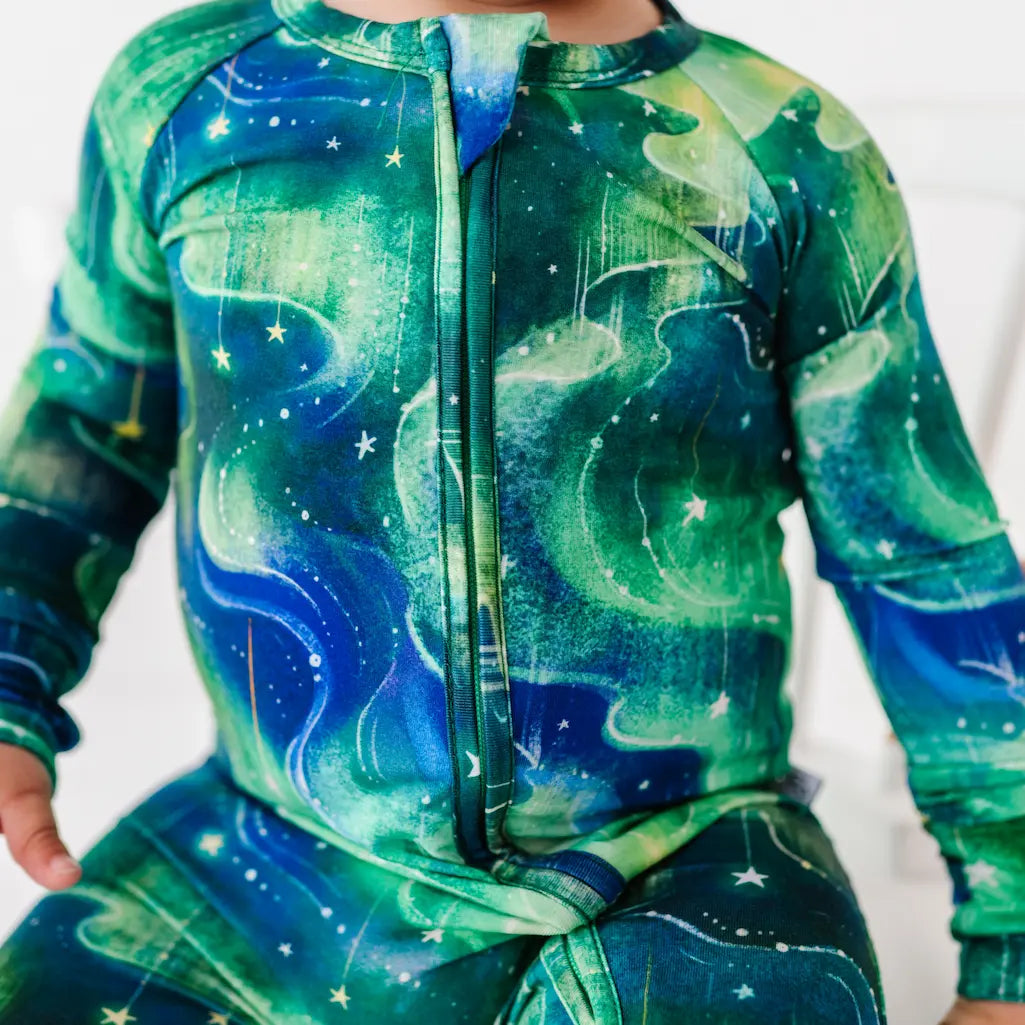 Child wearing a green and blue space-themed onesie with stars and celestial designs.