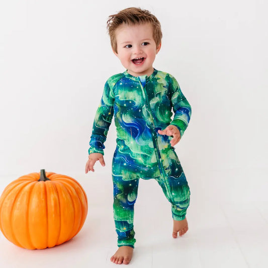 Child wearing a green and blue patterned onesie next to a pumpkin on a white background