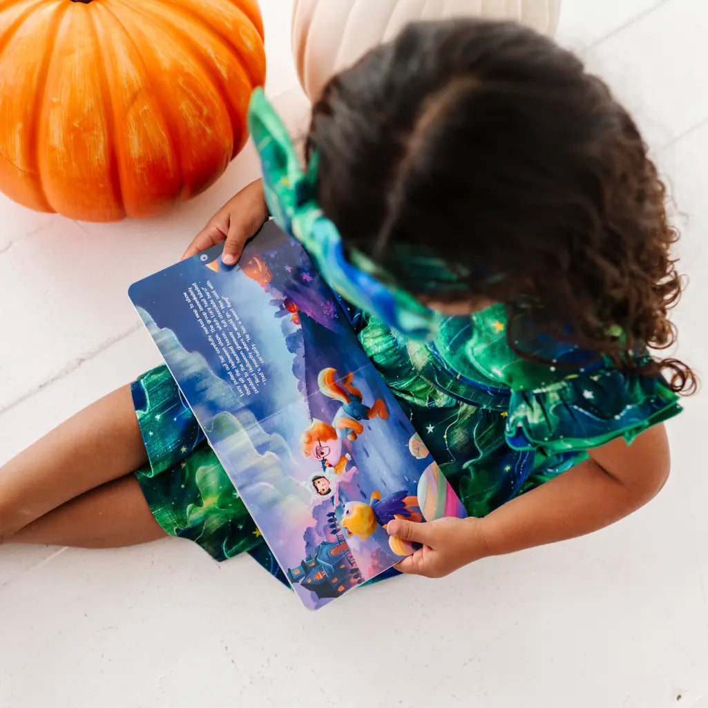 Child in a mermaid costume reading a book with a pumpkin nearby