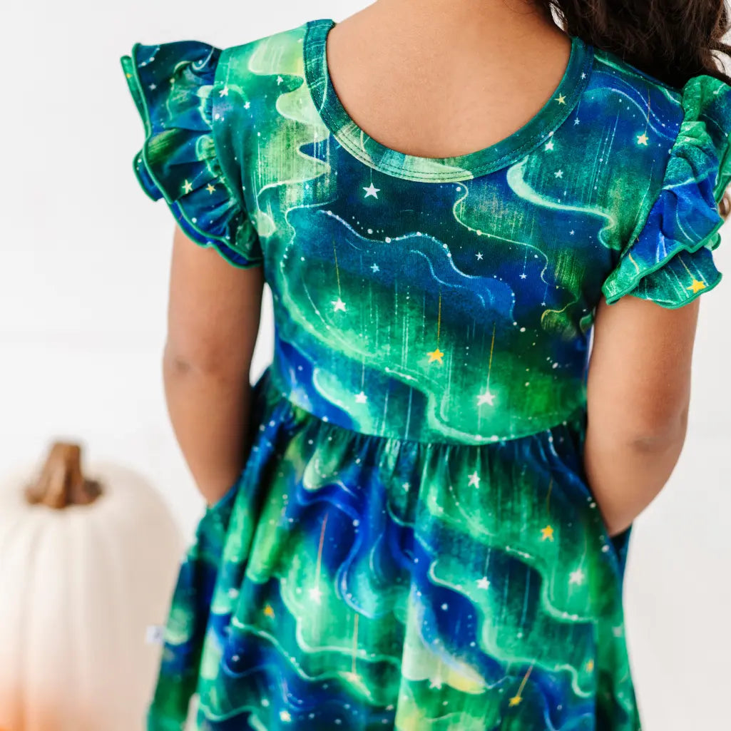 Child wearing a green and blue dress with celestial design, standing next to a white pumpkin.