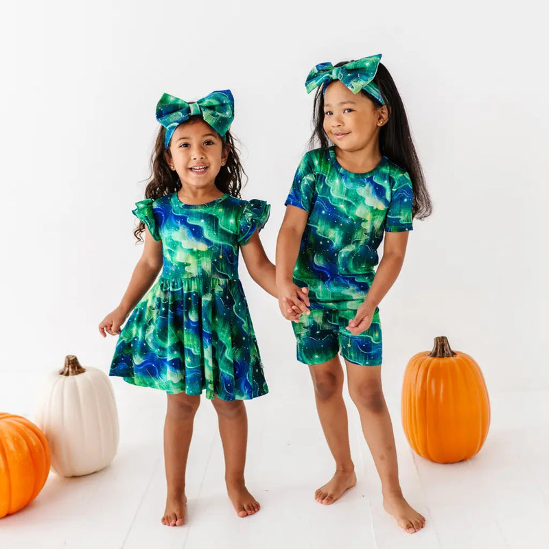Two children wearing matching green and blue outfits with pumpkins on a white background