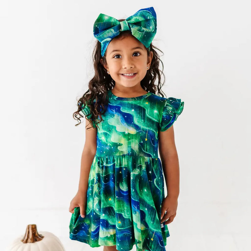Young girl wearing a green and blue dress with a matching bow on a white background