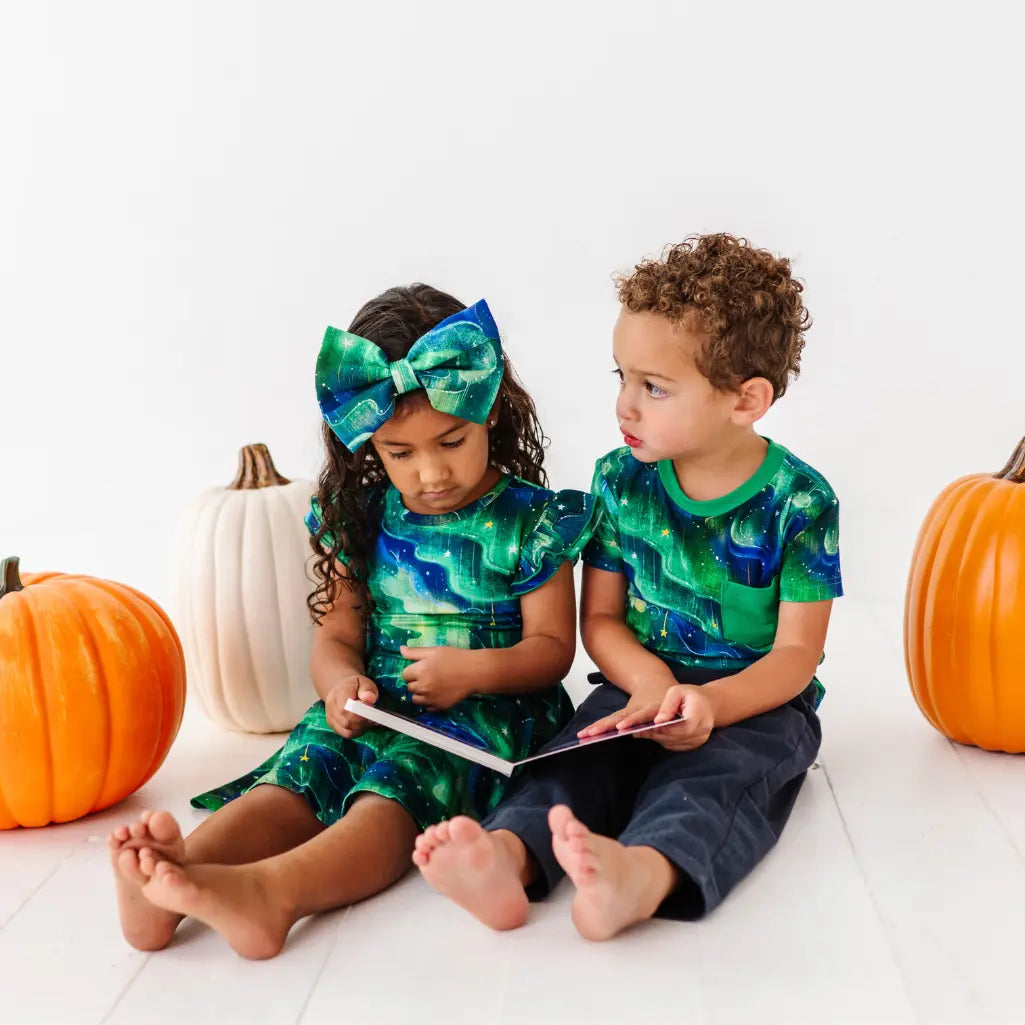 Two children in matching green and blue outfits with pumpkins on a white background