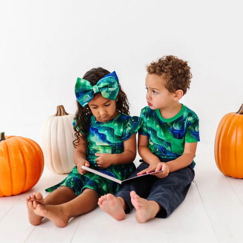 Two children in matching green and blue outfits with pumpkins on a white background