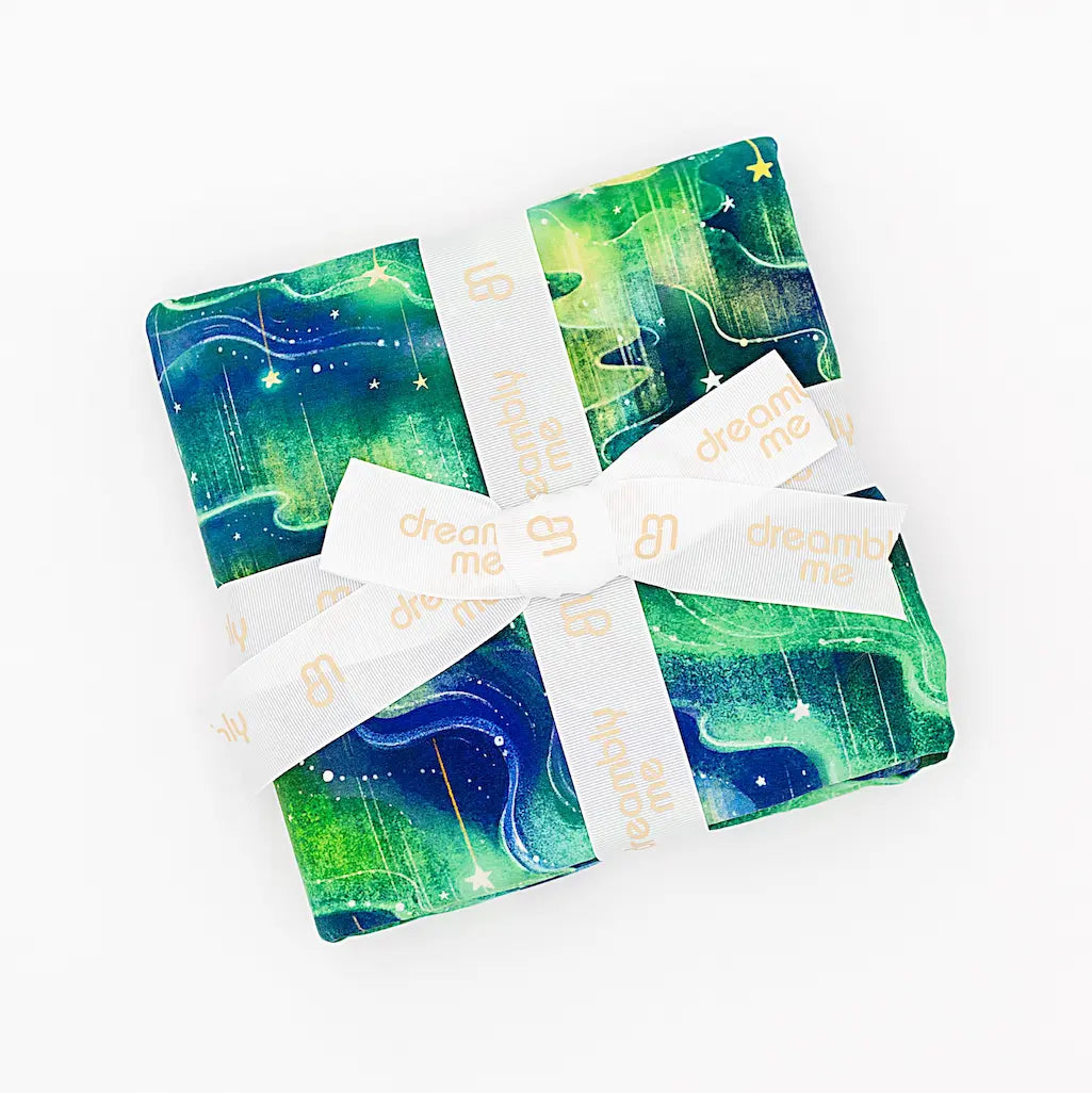 Green and blue patterned fabric folded and tied with a cream 'dream me' ribbon on a white background