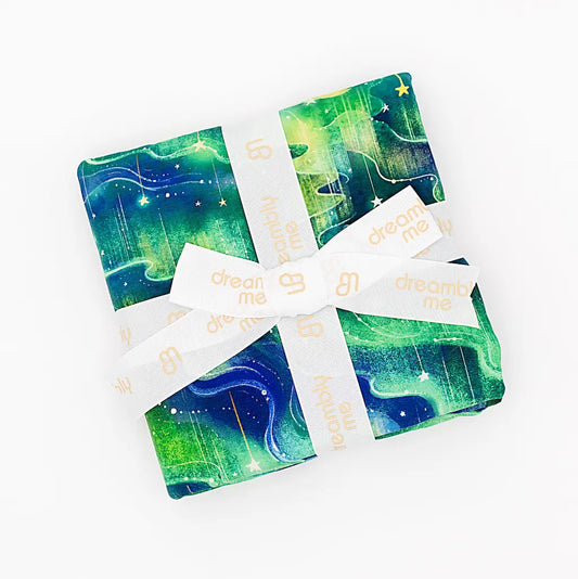Green and blue patterned fabric folded and tied with a cream 'dream me' ribbon on a white background