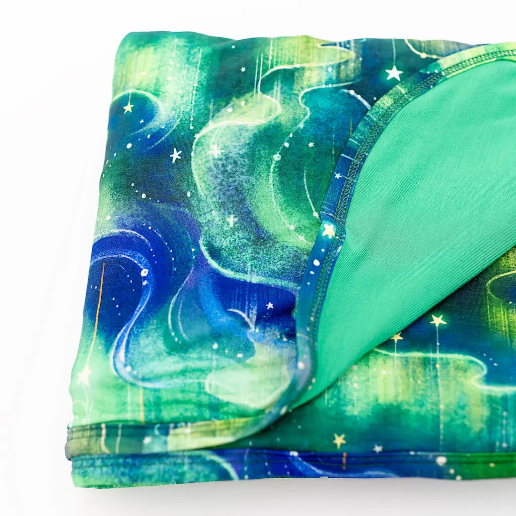 Folded green and blue blanket featuring a swirling cosmic pattern with stars on a white background
